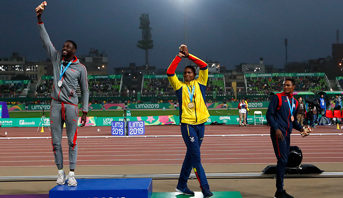 Silver medalist Jereem Richards of Trinidad and Tobago, right, walks away as gold medalist Alex Quinonez of Ecuador, center, and bronze medalist Yancarlos Martinez of Dominican Republic celebrate on the podium for the men's 200m during the athletics at the Pan American Games in Lima, Peru, Friday, Aug. 9, 2019. (AP Photo/Moises Castillo)